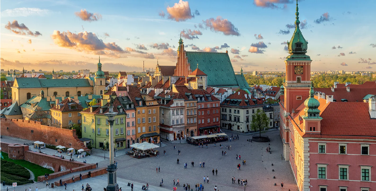 View of Castle Square in Warsaw, Poland, with colorful buildings, a clock tower, a cathedral roof, and people walking.